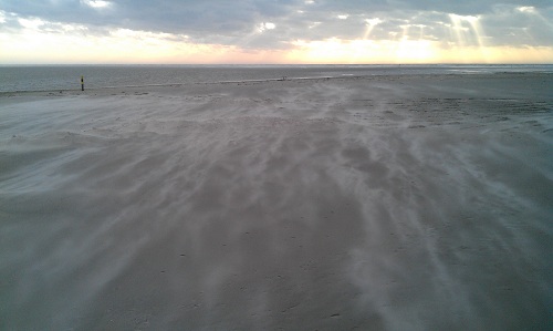 Wind weht Sand über den Strand