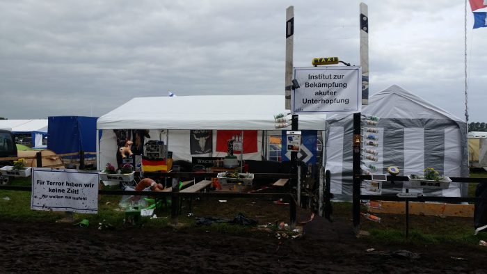 Ein typisches Camp beim Wacken Open Air: Pavillons mit Zaun davor und Schildern auf denen etwa "Institut zur bekämpfung akuter Unterhopfung" steht.