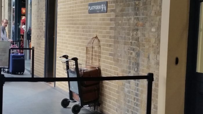 In einer Wand mit einem Schild "Platform 9 3/4" ist ein Gepäckwagen halb in der Wand verschwunden