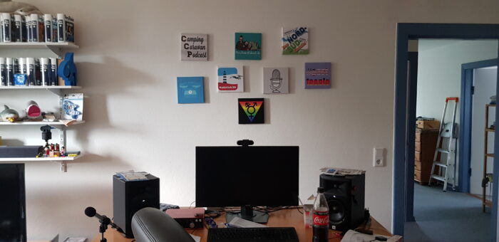 Die Logos aller Podcasts aus der Casa Schaarsa an der Wand über dem Schreibtisch.